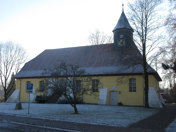 Ehemalige St. Jacobi-Kirche in Husum mit gelber Fassade, kleinem Türmchen und schneebedeckten Bäumen.