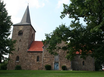 Kirche Windheim Alte Backsteinkirche in Windheim mit rotem Dach und spitzem Turm, umgeben von grünen Bäumen.