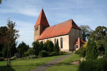 Die Willehadikirche in Eystrup mit rotem Dach und Turm umgeben von einem gepflegten Garten.