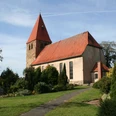 Die Willehadikirche in Eystrup mit rotem Dach und Turm umgeben von einem gepflegten Garten.