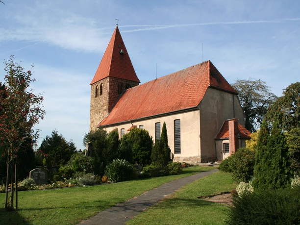 Willehadikirche in Eystrup Die Willehadikirche in Eystrup mit rotem Dach und Turm umgeben von einem gepflegten Garten.