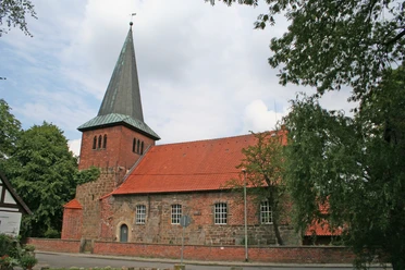Brick church with a striking pointed roof, surrounded by trees, against a cloudy sky in Holtorf.