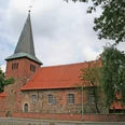 Kirche Holtorf Backsteinkirche mit markantem Spitzdach, umgeben von Bäumen, vor bewölktem Himmel in Holtorf.Brick church with a striking pointed roof, surrounded by trees, against a cloudy sky in Holtorf.Murstenskirke med et markant spidst tag, omgivet af træer, mod en overskyet himmel i Holtorf.Bakstenen kerk met een opvallend puntdak, omgeven door bomen, tegen een bewolkte lucht in Holtorf.
