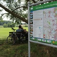 Radfahrer am Weser-Radweg Zwei Radfahrer pausieren an einer Bank auf einer grünen Wiese, neben einem Info-Schild am Weser-Radweg.