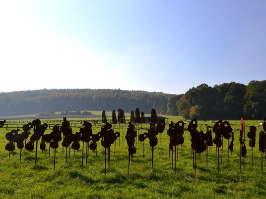 Encore Kunstinstallation im Freien mit zahlreichen dunklen Silhouetten vor einem Wald- und Feldhintergrund.