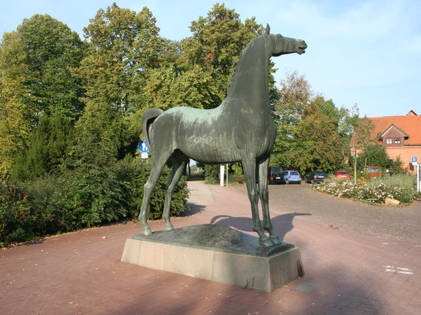 Wiehender Hengst Bronzestatue eines aufrecht stehenden, wiehenden Hengstes auf einem gepflasterten Platz, umgeben von Bäumen.