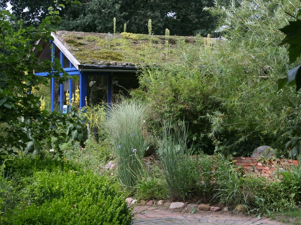 An educational garden with lush vegetation and a moss-covered roof in the background.