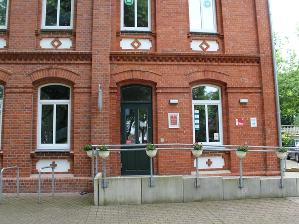 Red brick building of the Stolzenau tourist information office with barrier-free entrance and flower pots.