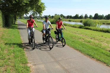 Radfahrer an der Weser Drei Radfahrer genießen eine sonnige Fahrt auf einem Radweg entlang der grünen Weserlandschaft.
