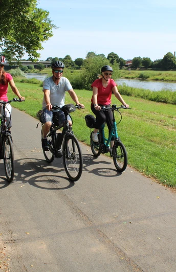 Radfahrer an der Weser Drei Radfahrer genießen eine sonnige Fahrt auf einem Radweg entlang der grünen Weserlandschaft.