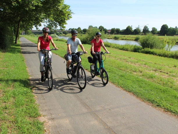 Radfahrer an der Weser Drei Radfahrer genießen eine sonnige Fahrt auf einem Radweg entlang der grünen Weserlandschaft.