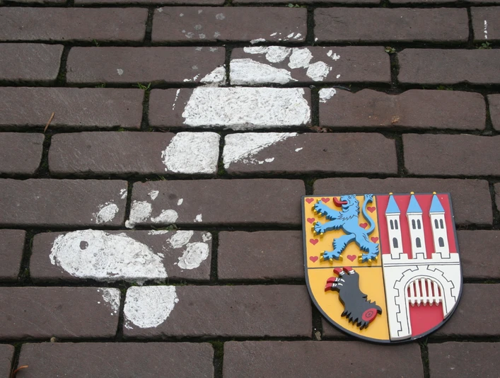 Ein Bärenfußabdruck aus weißer Farbe sowie ein farbenfrohes Stadtwappen zieren eine Pflasterfläche.A bear's footprint in white paint and a colorful city coat of arms adorn a paved area.Et bjørnefodaftryk i hvid maling og et farverigt byvåben pryder et asfalteret område.Een voetafdruk van een beer in witte verf en een kleurrijk stadswapen sieren een geplaveid gebied.