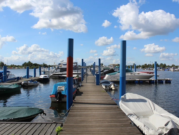 Wieltsee Weyhe Holzsteg führt durch eine Boots-Marina mit verschiedenen Motorbooten bei blauem Himmel und Wolken.Wooden jetty leads through a boat marina with various motorboats under a blue sky and clouds.En træbrygge fører gennem en bådhavn med forskellige motorbåde under en blå himmel og skyer.Een houten steiger leidt door een jachthaven met verschillende motorboten onder een blauwe hemel en wolken.
