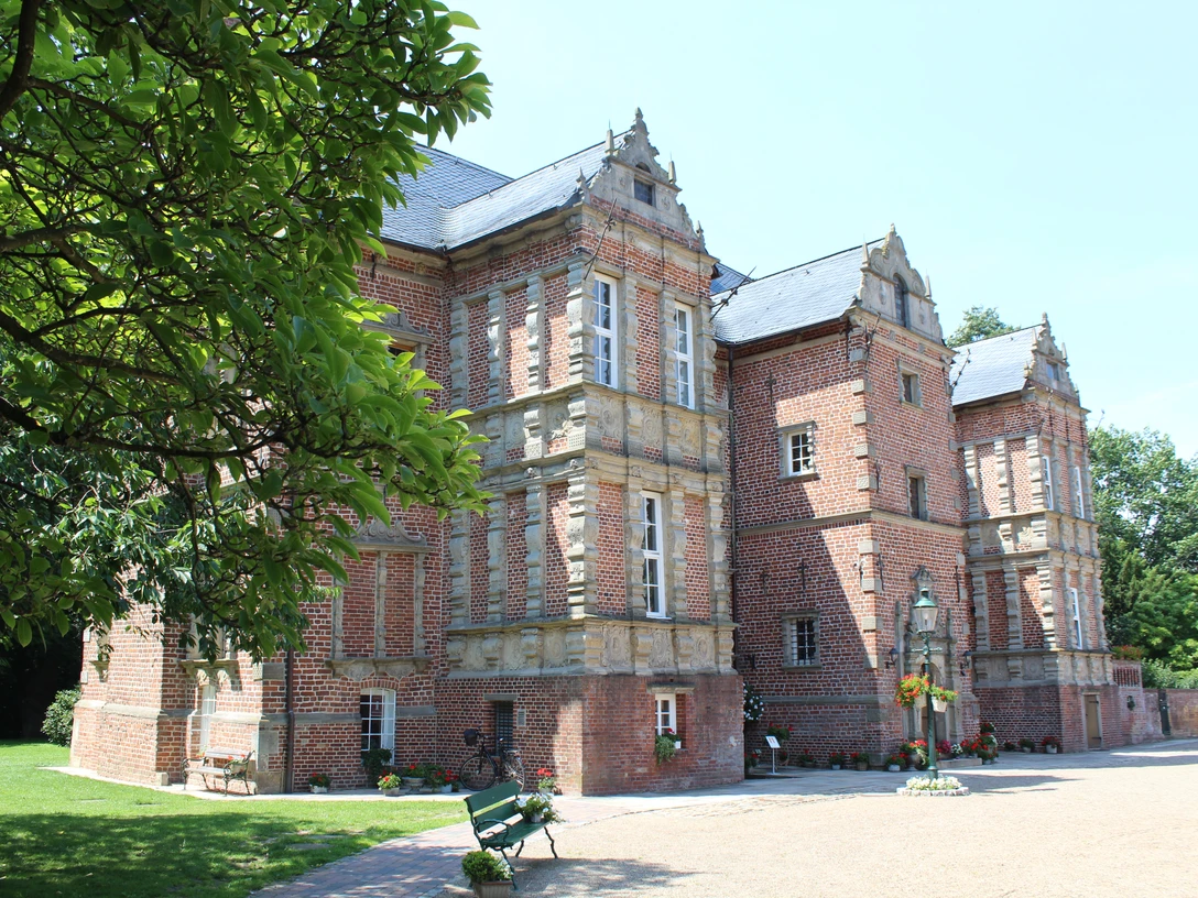 Historisches Backsteinschloss mit grüner Umgebung und blauen Türen, beleuchtet von sommerlichem Sonnenlicht.