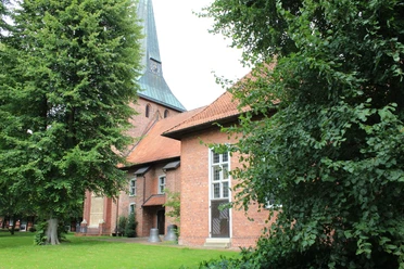 Brick church with a green pointed roof, flanked by large deciduous trees, on a well-tended lawn.