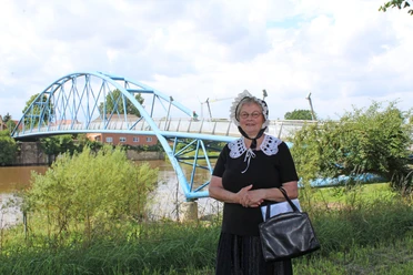 Gewandete Stadtführerin Nienburg Eine Frau in historischer Tracht steht vor einer blauen Brücke an einem Flussufer in Nienburg.
