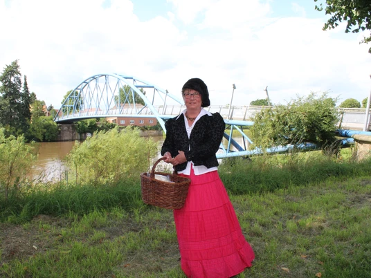 Eine Stadtführerin in historischer Kleidung steht mit einem Korb an der Weserbrücke in Nienburg.