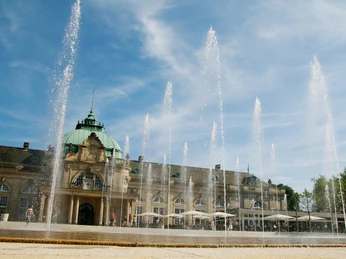 Leander Außenbereich (c) GOP Variete.jpg Auf dem Bild ist der Außenbereich des Leanders zu sehen, mit Blick auf das Kaiserpalais. Die Fontänen sind eingeschaltet, und das Wasser spritzt in die Luft.