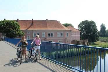 Zwei Radfahrer auf einer Brücke vor dem historischen Grafenschloss Hoya an einem sonnigen Tag.