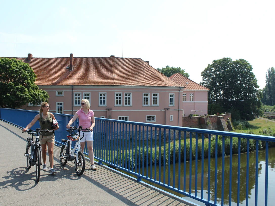 Radfahrer am Grafenschloss Hoya Zwei Radfahrer auf einer Brücke vor dem historischen Grafenschloss Hoya an einem sonnigen Tag.