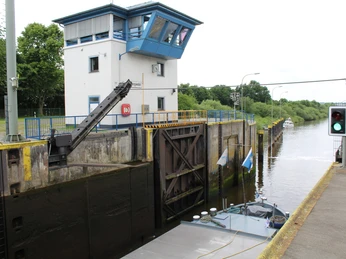 Schleuse Langwedel am Weserfluss mit modernem Kontrollturm und einem Frachtschiff auf ruhigem Wasser.