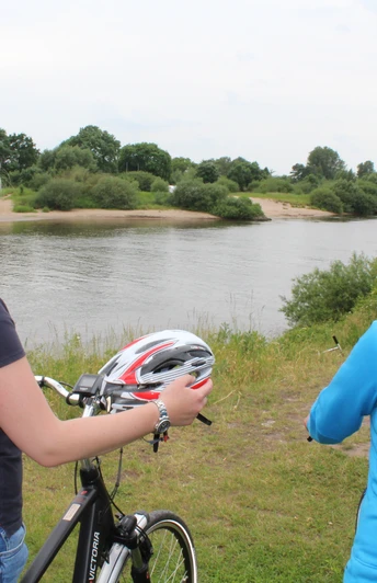 Zwei Frauen stehen mit Fahrrädern am Weserufer, blicken auf den ruhigen Fluss und die Natur.