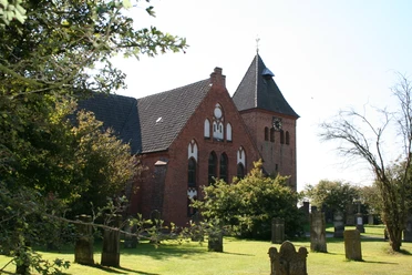 St.-Sigismund-Kirche in Daverden Backstein-Kirche in ländlicher Anlage mit grünem Rasen, Bäumen und altem Kirchturm mit Uhr.