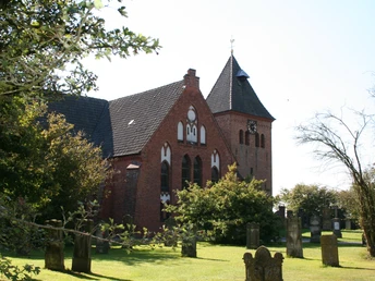 St.-Sigismund-Kirche in Daverden Backstein-Kirche in ländlicher Anlage mit grünem Rasen, Bäumen und altem Kirchturm mit Uhr.