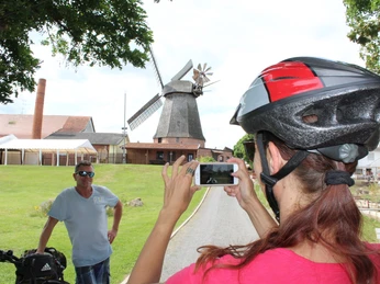 Büschings Mühle Ein Radfahrer posiert vor der historischen Büschings Mühle, während eine Frau mit Helm ein Foto macht.
