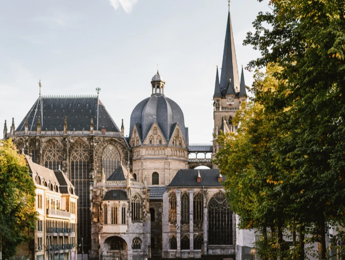 Blick über den Katschhof auf den Dom, rechts und links stehen grüne Bäume.