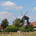 Windmühle Loccum Historische Windmühle, umgeben von grüner Vegetation und roten Ziegeldächern unter blauem Himmel.