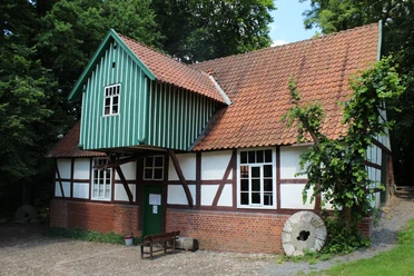 Plaggen Mühle Döhren Fachwerkhaus der Plaggen Mühle Döhren mit backsteinrotem Dach, umrahmt von dichtem Grün der Natur.