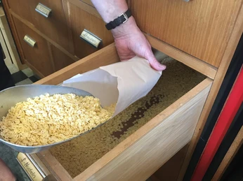 Tante Emma Neuenkruge Nudeln.jpg Eine Hand füllt vorsichtig Nudeln aus einer großen Schaufel in eine offene Schublade.