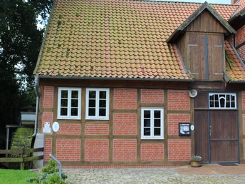 Wassermühle Bruchmühlen Fachwerkgebäude mit roten Ziegelwänden und Holztor, daneben drei weiße Fenster. Links ein Holzbalken.