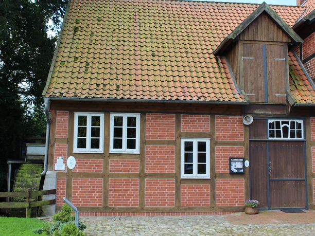 Wassermühle Bruchmühlen Fachwerkgebäude mit roten Ziegelwänden und Holztor, daneben drei weiße Fenster. Links ein Holzbalken.