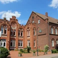 Bauschule Rehburg Historisches Backsteingebäude mit Spitzfenstern und Turmspitze, flankiert von Blumendekorationen.