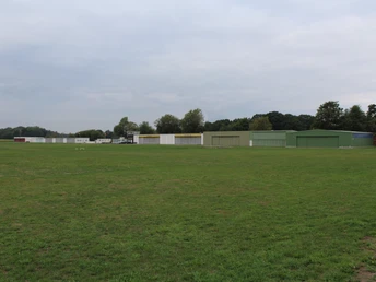 Flugplatz Holzbalge Grüne Landebahn mit mehreren Hangars im Hintergrund, umgeben von Bäumen und weitreichendem Himmel.