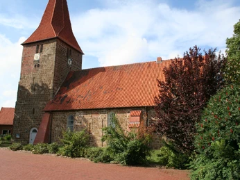 St.-Bartholomäus-Kirche in Balge Historische Backsteinkirche mit markantem Turm und rotem Ziegeldach, umgeben von Pflanzen.