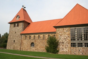 Historic brick church with red tiled roofs and striking church tower, nestled in a green meadow.