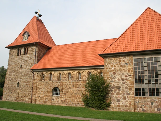 Historic brick church with red tiled roofs and striking church tower, nestled in a green meadow.
