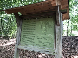 Information board in the forest with historical map and text about the "Alte Schanze" on Oyler Berg in the background.