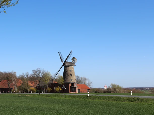 Historic Petershagen pot mill with windmill wings, surrounded by red buildings and green countryside.