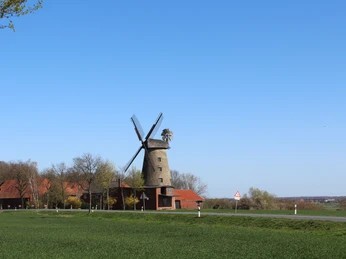 Pottmühle Petershagen Historische Pottmühle Petershagen mit Windmühlenflügeln, umgeben von roten Gebäuden und grüner Landschaft.
