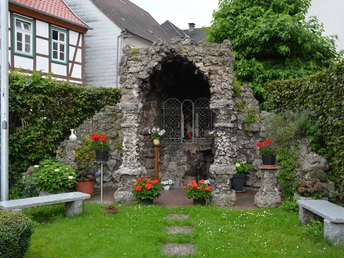 Steinarchitektur einer kleinen Kapelle mit drei Bögen, von Pflanzen umgeben, auf grünem Gelände.