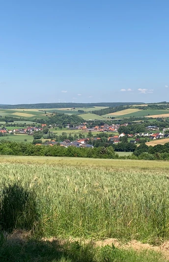Weite Felder und sanfte Hügel umgeben das Dorf Erkeln an einem sonnigen, wolkenlosen Tag.