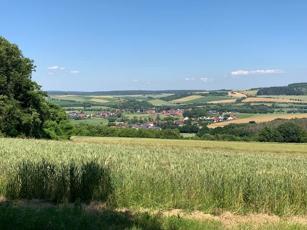 Blick auf Erkeln Weite Felder und sanfte Hügel umgeben das Dorf Erkeln an einem sonnigen, wolkenlosen Tag.