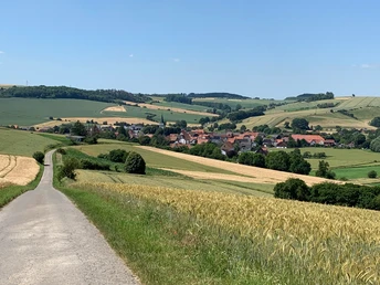Blick auf Erkeln Ländliche Landschaft mit einem Dorf inmitten sanfter Hügel und Felder unter einem klaren blauen Himmel.