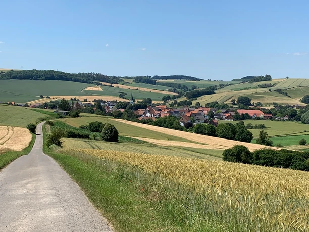 Blick auf Erkeln Ländliche Landschaft mit einem Dorf inmitten sanfter Hügel und Felder unter einem klaren blauen Himmel.