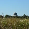 Radarstation Auenhausen Radarstation Auenhausen: Eine moderne Kuppel hebt sich hinter einer Wiese mit Gräsern und Wildblumen ab.