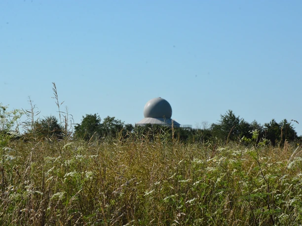 Radarstation Auenhausen Radarstation Auenhausen: Eine moderne Kuppel hebt sich hinter einer Wiese mit Gräsern und Wildblumen ab.
